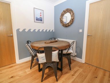 A dining area with a round wooden table surrounded by four metal chairs with cushions and a wall mirror at 8 Pen Llanw Tides Reach in Rhosneigr