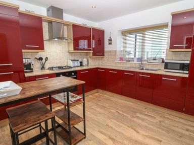 A kitchen with red cabinets wooden floor and a small wooden table with stools at 8 Pen Llanw Tides Reach in Rhosneigr