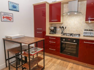 A kitchen with red cabinets a gas stove oven toaster coffee maker and a wooden table with stools at 8 Pen Llanw Tides Reach in Rhosneigr