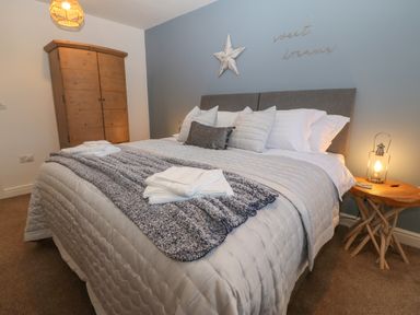 A bedroom with a bed and wooden wardrobe and bedside table with lamp at 8 Pen Llanw Tides Reach in Rhosneigr