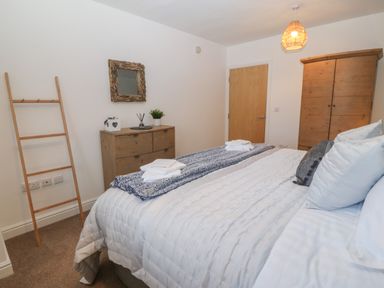 A bedroom with a bed a wooden dresser a wooden wardrobe a ladder and a mirror at 8 Pen Llanw Tides Reach in Rhosneigr