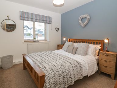 A bedroom with a wooden bed frame and knitted blanket at 8 Pen Llanw Tides Reach in Rhosneigr