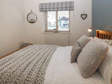 A bedroom with a bed featuring textured pillows and a knitted throw near a window with blinds at 8 Pen Llanw Tides Reach in Rhosneigr