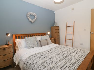 A bedroom with a wooden bed frame and knitted bedding at 8 Pen Llanw Tides Reach in Rhosneigr