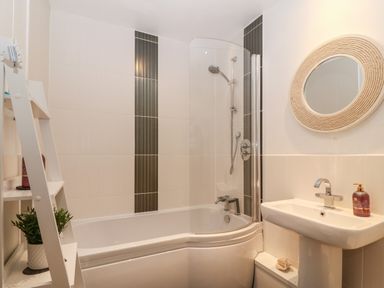 A bathroom with a bathtub shower combination sink and a round mirror at 8 Pen Llanw Tides Reach in Rhosneigr