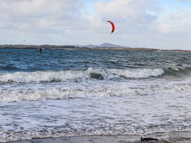 A beach with waves and a person kite surfing on the water at 8 Pen Llanw Tides Reach in Rhosneigr