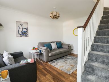 A living room with two sofas a small table with fruit a rug and carpeted stairs at Little Tern Brewers Quay Harbour