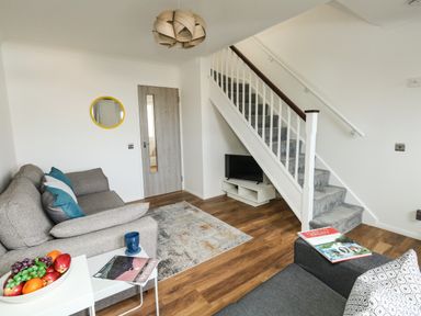 A living room with gray sofas a small white table with fruit a gray carpet wooden floor stairs and a television at Little Tern in Brewers Quay Harbour