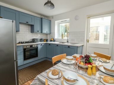 A kitchen with blue cabinets a dining table set with bowls plates and fruit at Little Tern in Brewers Quay Harbour
