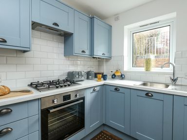 A kitchen with blue cabinets a built in oven a gas stove a sink and window at Little Tern Brewers Quay Harbour
