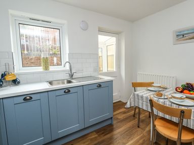 A kitchen with blue cabinets a sink and a dining table with chairs and fruit at Little Tern Brewers Quay Harbour