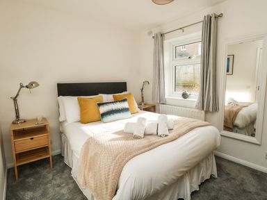 A bedroom with a bed a nightstand with a lamp and a window with curtains at Little Tern in Brewers Quay Harbour