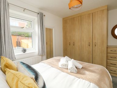 A bedroom with a bed with towels on it a window with curtains and built in wooden wardrobes at Little Tern Brewers Quay Harbour