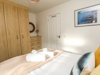 A bedroom with a bed with pillows and towels a wooden wardrobe a chest of drawers with a mirror and a framed picture on the wall at Little Tern Brewers Quay Harbour