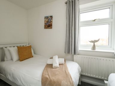 A bedroom with a bed a window striped curtains and a small whale tail ornament on the window sill at Little Tern in Brewers Quay Harbour