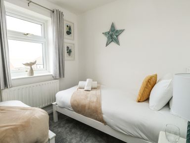 A bedroom with two single beds a window with curtains and wall decorations at Little Tern Brewers Quay Harbour