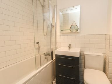 A bathroom with a bathtub and shower, a sink with a cabinet below, a mirror above the sink and a toilet at Little Tern in Brewers Quay Harbour