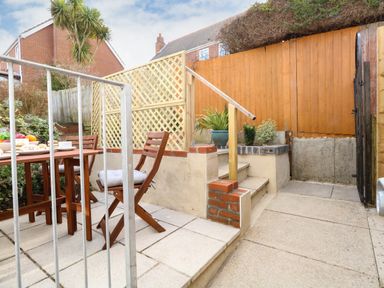 An outdoor patio area with wooden table and chairs and potted plants next to stairs and wooden fence