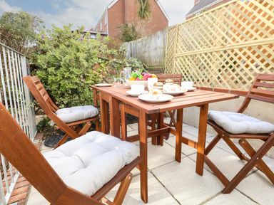 An outdoor patio with a wooden table and four chairs with cushions and tableware at Little Tern in Brewers Quay Harbour