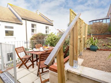 An outdoor patio area with a wooden table and chairs set with dishes and fruit at Little Tern Brewers Quay Harbour