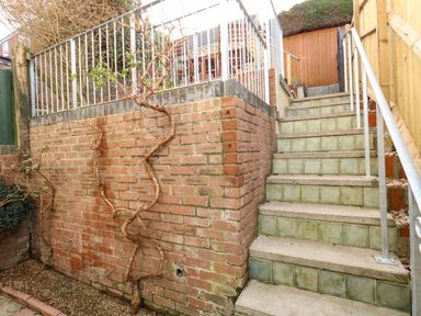 An outdoor tiled staircase with metal railings next to a brick wall with climbing plants