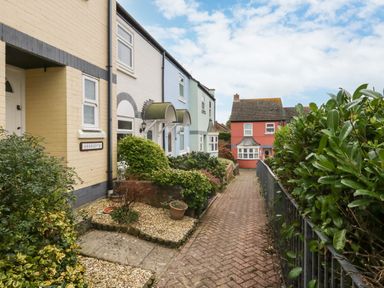 A row of pastel-colored houses along a pathway with plants and bushes near the entrance at Little Tern Brewers Quay Harbour