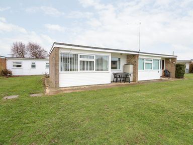 A single story building with patio furniture on a grassy lawn at Chalet 12 in Hemsby