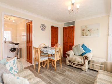 A living room with a dining table and chairs adjacent to a kitchen and armchairs at Chalet 12 in Hemsby
