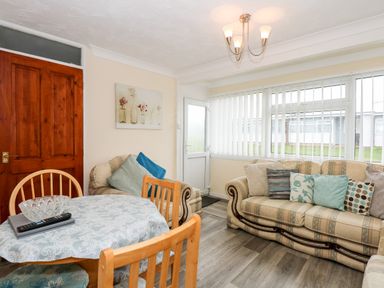 A living room with two sofas a dining table with chairs and a door with windows at Chalet 12 in Hemsby