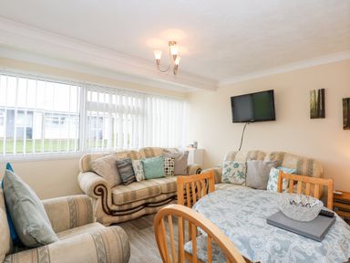 A living room with sofas dining table with tablecloth and a wall mounted television at Chalet 12 in Hemsby