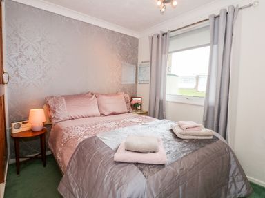 A bedroom with a double bed towels on bed a window with curtains and a bedside table with a lamp at Chalet 12 in Hemsby