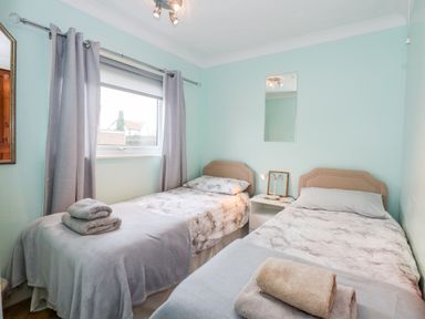 A bedroom with two single beds a window with curtains and a nightstand between the beds at Chalet 12 in Hemsby