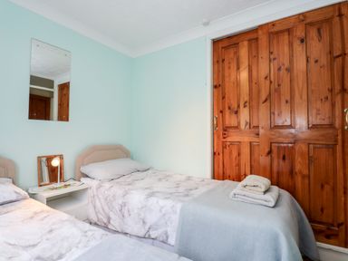 A bedroom with two single beds a nightstand with a lamp a wall mirror and wooden closet doors at Chalet 12 in Hemsby