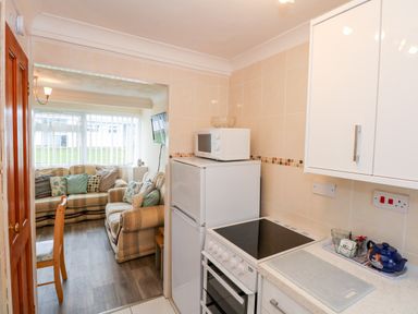 A kitchen with a stove microwave refrigerator and cabinets leading to a living room with sofas and cushions at Chalet 12 in Hemsby