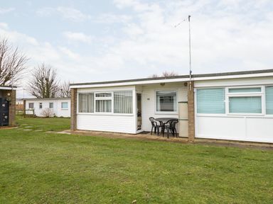 A single-story building with a patio table and chairs outside on grass at Chalet 12 in Hemsby