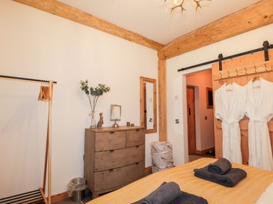 A bedroom with a wooden chest of drawers a clothing rack a mirror and two white bathrobes hanging on a wooden door at Pine Marten Lodge Dulnain Bridge near Nethy Bridge