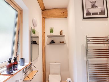 A bathroom with a toilet a towel rack two shelves with decorations and a window with toiletries at Pine Marten Lodge Dulnain Bridge near Nethy Bridge