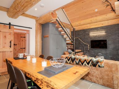 A living and dining area with a wooden dining table and chairs a couch with a patterned throw and a mounted TV on a slate accent wall at Pine Marten Lodge Dulnain Bridge near Nethy Bridge