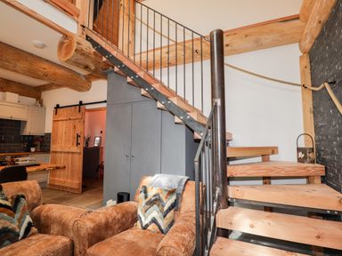 A room with wooden staircase brown armchairs and kitchen visible through a wooden sliding door at Pine Marten Lodge in Dulnain Bridge near Nethy Bridge