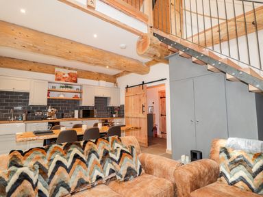 An open-plan kitchen and living area with wooden beams a staircase and patterned cushions on sofas at Pine Marten Lodge in Dulnain Bridge near Nethy Bridge