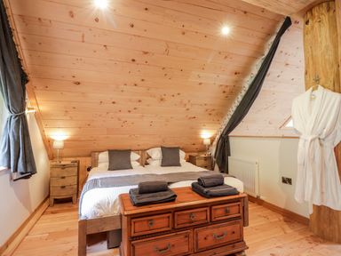 A bedroom with two single beds, wooden furniture, gray curtains and towels, and a white robe hanging on a wooden beam at Pine Marten Lodge Dulnain Bridge near Nethy Bridge