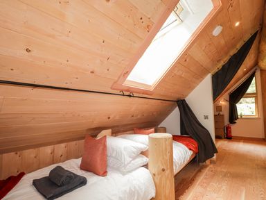 A bedroom with a wooden bed under a slanted wooden ceiling with a skylight and a window with dark curtains at Pine Marten Lodge in Dulnain Bridge near Nethy Bridge