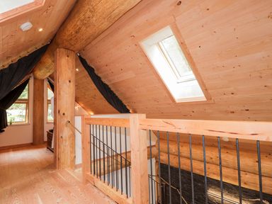 An upstairs wooden hallway with a railing overlooking stairs and a skylight window at Pine Marten Lodge in Dulnain Bridge near Nethy Bridge