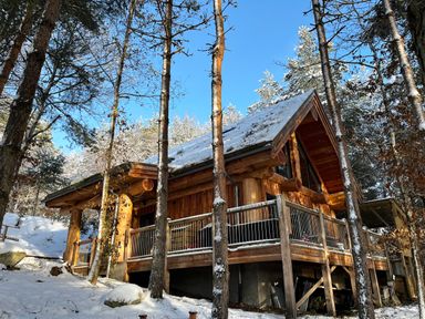 A wooden cabin in a snowy forest with a deck and railing at Pine Marten Lodge in Dulnain Bridge near Nethy Bridge