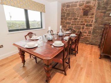 A dining room with a wooden table set with white dishes glassware and two candle holders against a stone wall at Shepherds House in Lowick