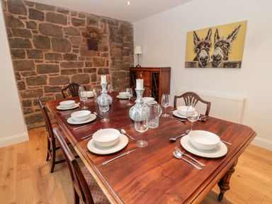 A dining room with a wooden table set for six and a brick wall at Shepherds House in Lowick
