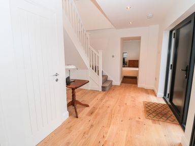 An entryway with wooden floor a small wooden table with a lamp under stairs and a black door at Shepherds House in Lowick