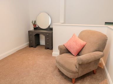 A corner with a gray vanity table with a round mirror and a plant and a brown armchair with a pink pillow at Shepherds House in Lowick