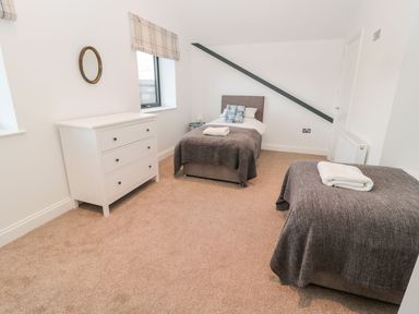 A bedroom with two single beds covered with gray blankets a white chest of drawers and a round wall mirror at Shepherds House in Lowick