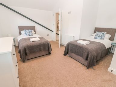 A bedroom with two single beds a dresser and an open door at Shepherds House in Lowick